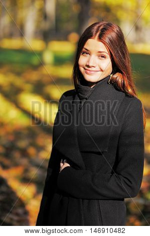 Cute smiling, brown-eyed girl with long brown hair in the autumn forest looking at you.