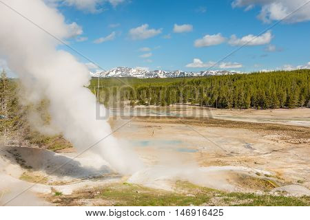 Steamboat geyser in Norris Basin in Yellowstone National Park with hot steam, vapor, blue hot springs and mountains