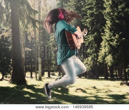 Girl with heaphones jumping and playing guitar in the woods