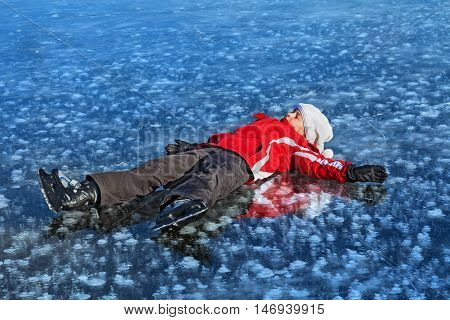 Young girl with ice skates resting on the frozen lake surface in the bright sunshine - copy space