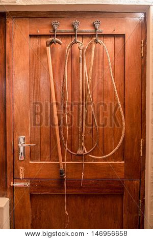 Two whips and a walking stick hang from hooks on the back of a farmers wooden door.