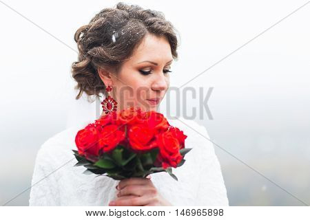 winter bride in beautirul fur shawl holding bouquet of red roses