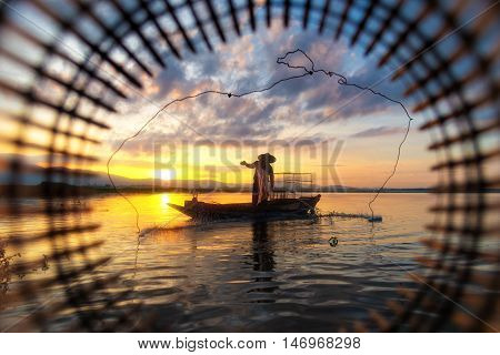Fisherman on wooden boat casting a net for catching fish in morning.