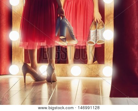 Cute little fashionista. Happy child girl try on outfits and mom's shoes looking at mirror.