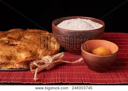 A Bowl With Flour And Apricot Cake On A Wooden Background On Black