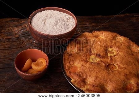 A Bowl With Flour And Apricot Cake On A Wooden Background On Black