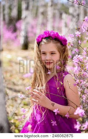 Portrait Of Child With A Long Blond Hair Stands Among The Ledum And Birch In A Pink Dress And Smilin