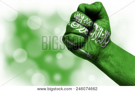 Flag Of Saudi Arabia Painted On Male Fist, Strength, Power, Concept Of Conflict. On A Blurred Backgr