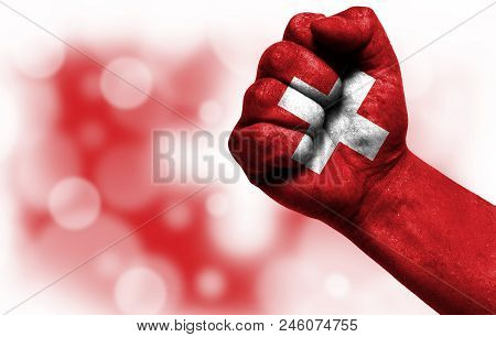 Flag Of Switzerland Painted On Male Fist, Strength, Power, Concept Of Conflict. On A Blurred Backgro