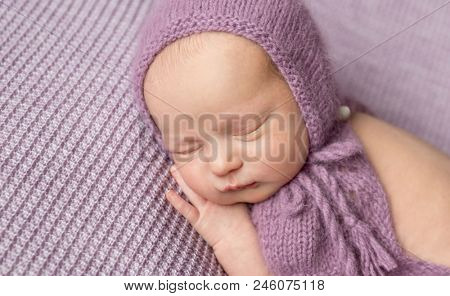 Cute little girl in purple knitted bonnet sleeping on her side