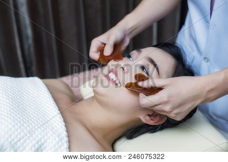 Asian Young Woman Have Face Guasha Treatment At Asian Beauty Clinic; Undergoing Acupuncture Treatmen