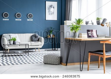 Dark Blue Living Room Interior With Three Clocks, Simple Poster, Bright Sofa And Home Office Corner