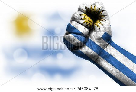 Flag Of Uruguay Drawn On Male Fist, Strength, Power, Concept Of Conflict. On A Blurred Background Wi