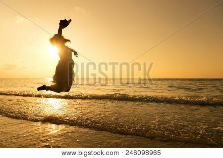 Silhouette Of Pretty Woman Wear White Dress Is Jumping And Relax On Beach. Positive Emotions. Summer