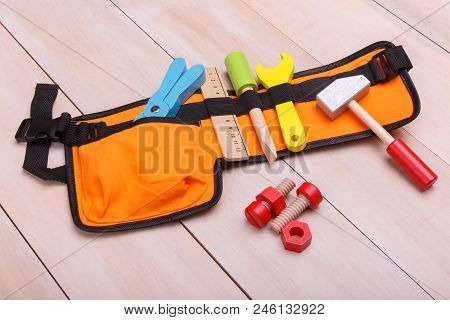 An Orange Bag With Such Toy Instruments As Ruler Pliers Hammer And Screwdriver Is Situated On A Wood