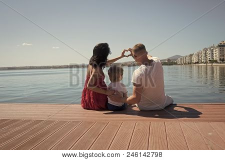 Happy Full-fledged Family. Parents With Son Sit On Seafront, Rear View. Mother And Father Making Hea