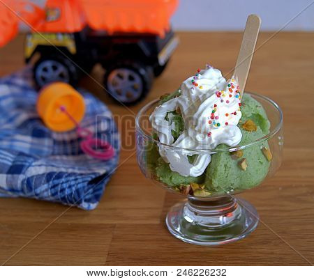 Frozen Yogurt Or Natural Green Ice Cream In Balls, With Pistachios, Whipped Cream And A Colorful Spr