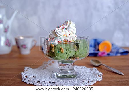 Frozen yogurt or natural green ice cream in balls, with pistachios, whipped cream and a colorful spr