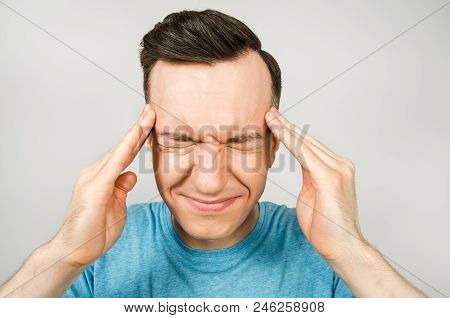 Young Guy With Headache Dressed In A Blue T-shirt On A Light Background.