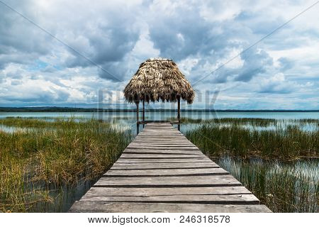 Hut With Straw Roof At The Dock Along The Lake Shore With Dark Blue Cloudscape And Sunshine, El Rema