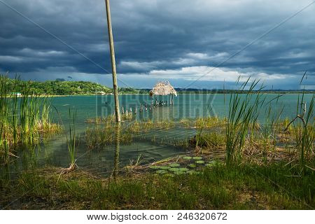 View To Village With Dock Along The Lake Shore With Birds Sitting On Sticks, El Remate, Peten, Guate