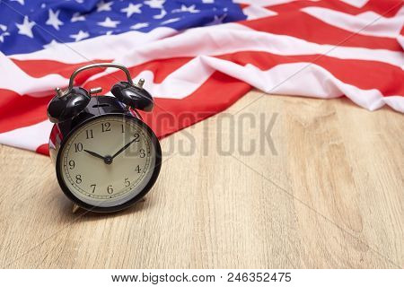 National flag of America and black alarm clock on old wooden background