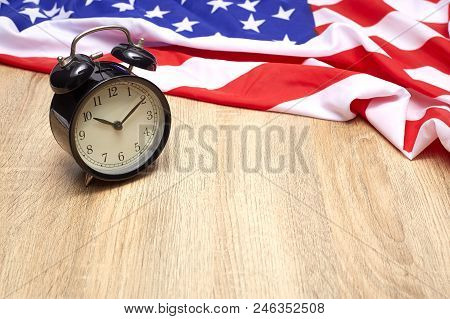 National Flag Of America And Black Alarm Clock On Old Wooden Background