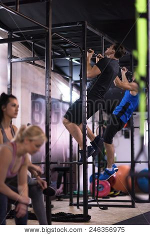 group of young muscular athletes doing pull ups on the horizontal bar as part of Cross fitness Training