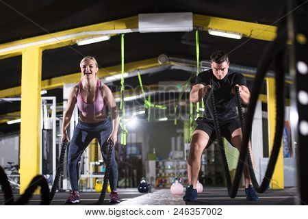 young fit sports couple working out in functional training gym doing  battle ropes cross fitness exercise