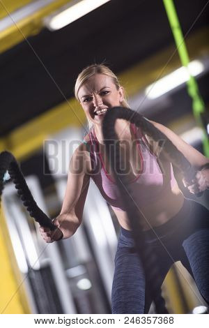 young fit athlete woman working out in functional training gym doing  battle ropes exercise as part of cross fitness training