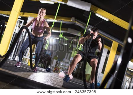 young fit sports couple working out in functional training gym doing  battle ropes cross fitness exercise