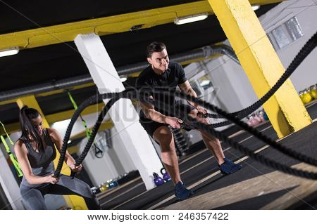 young fit sports couple working out in functional training gym doing  battle ropes cross fitness exercise