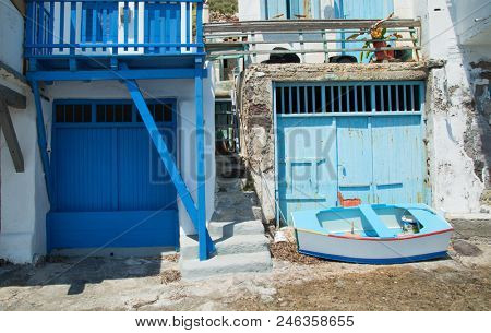 Blue fishing boat in front of a house with blue doors in Klima village in Milos island in Greece