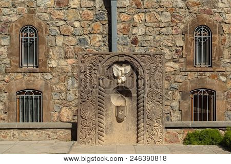 Armenian Stone Monument With A Drinking Fountain On The Background Of A Building Made Of Stones With