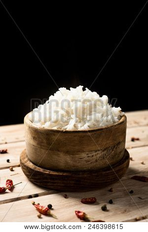 closeup of a boxwood bowl with some cooked long grain rice, on a rustic wooden table, against a black background, with some blank space on top