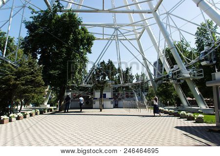 Clean White Ferris Wheel Over Blue Sky And Branches Of Trees.platform Landing People On The Ferris W