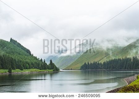 View Of A Beautlful Lake Talla In Scottish Borders With Green Hills Covered By Thick Rainy Clouds.