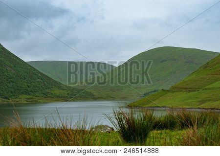 View Of A Beautlful Lake Talla In Scottish Borders With Green Hills Covered By Thick Rainy Clouds.