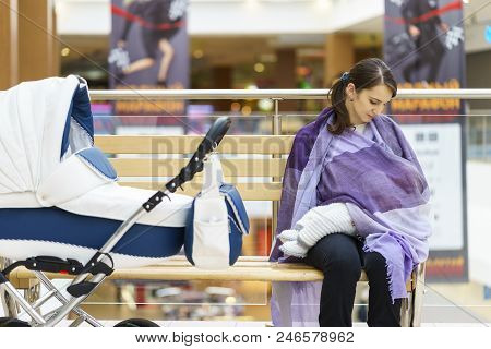 Young European Woman With Violet Stole Is Breastfeeding Her Little Child Close To White Baby Carriag
