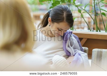 Young European Woman With Violet Stole Is Breastfeeding Her Little Child Close To White Baby Carriag