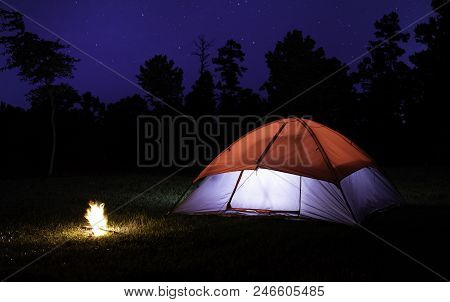 Small Campfire Next To Lit Tent With Stars In The Sky Above