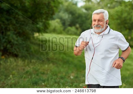 Smiling Running Old Man In Green City Park. Smiling, Feeling Good. Sport Lifestyle. Wearing Classic 