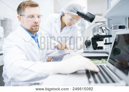 Side View Of Male Microbiologist In White Laboratory Coat Typing On Laptop Keyboard Data Received Du