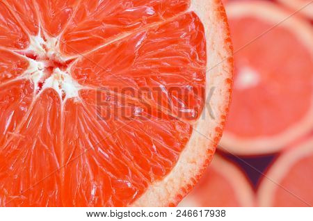 Top View Of A Fragment Of The Red Grapefruit Slice On The Background Of Many Blurred Grapefruit Slic