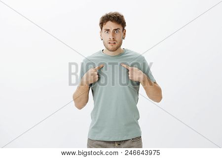Studio Shot Of Frustrated Angry Young Man With Bristle In T-shirt And Earrings, Pointing At Himself 