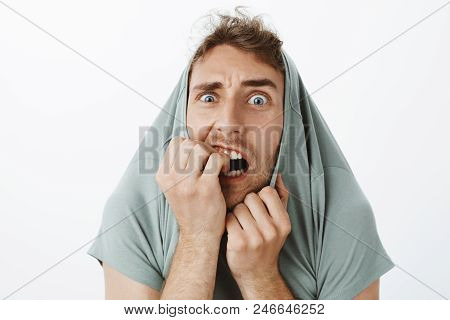 Indoor Shot Of Funny Scared Caucasian Guy With Bristle, Pulling T-shirt On Head And Staring With Pop