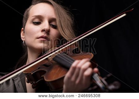 Young Woman With Half Of Her Hair Shaved While Playing A Baroque Violin On A Black Background