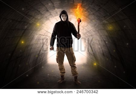 Ugly man with burning flambeau walking in a dark tunnel