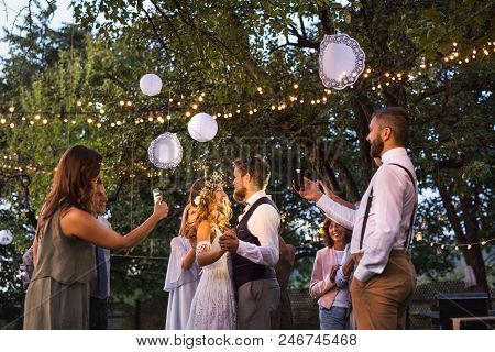 Guests With Smartphones Taking Photo Of A Dancing Bride And Groom At Wedding Reception Outside. An E
