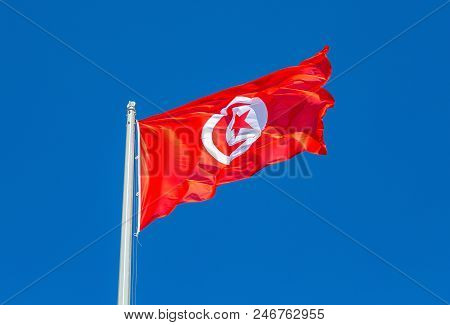 Flag Of Tunisia Waving In The Wind Against The Blue Sky